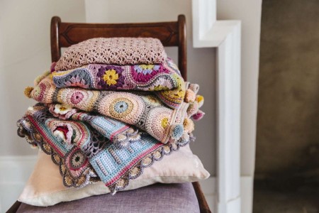 A pile of colourful heirloom handmade crocheted blankets on an antique chair 