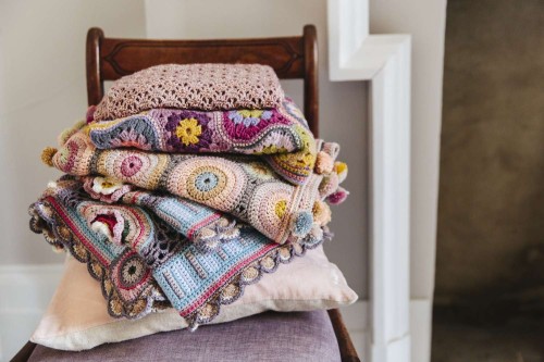 A pile of colourful heirloom handmade crocheted blankets on an antique chair 