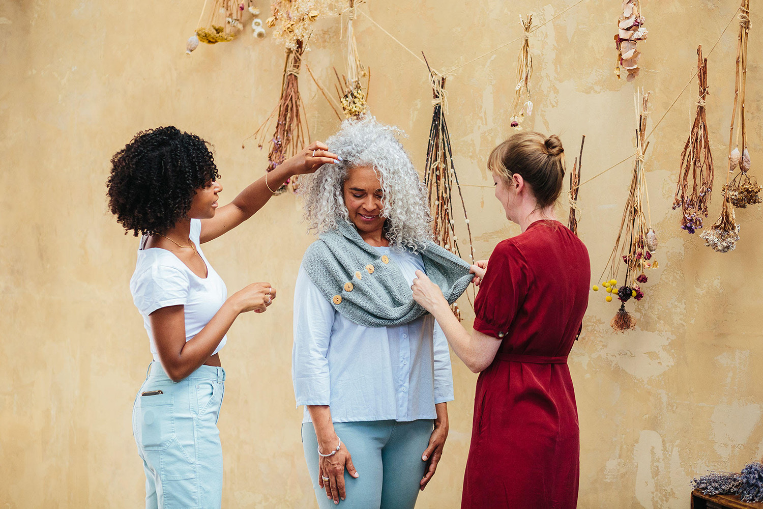Women styling handmade knitwear in a creative studio with dried flowers on display