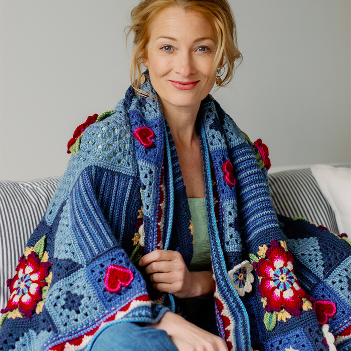 Smiling woman wrapped in a rich blue crochet blanket with heart and flower details 